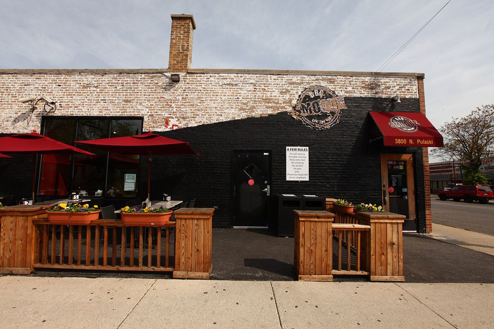 A brown wooden fence separates a low, dark-looking building from the sidewalk. Red awning hangs off the building.