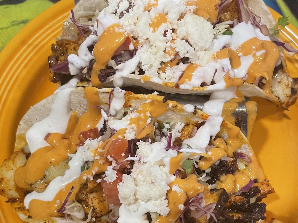 A closeup of two octopus tacos drizzled in sauce and cheese.