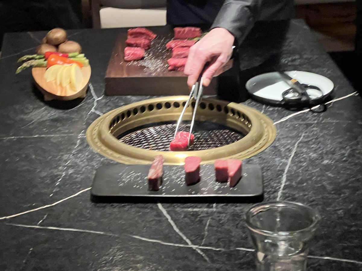 A hand holding tongs over a table grill with raw beef.