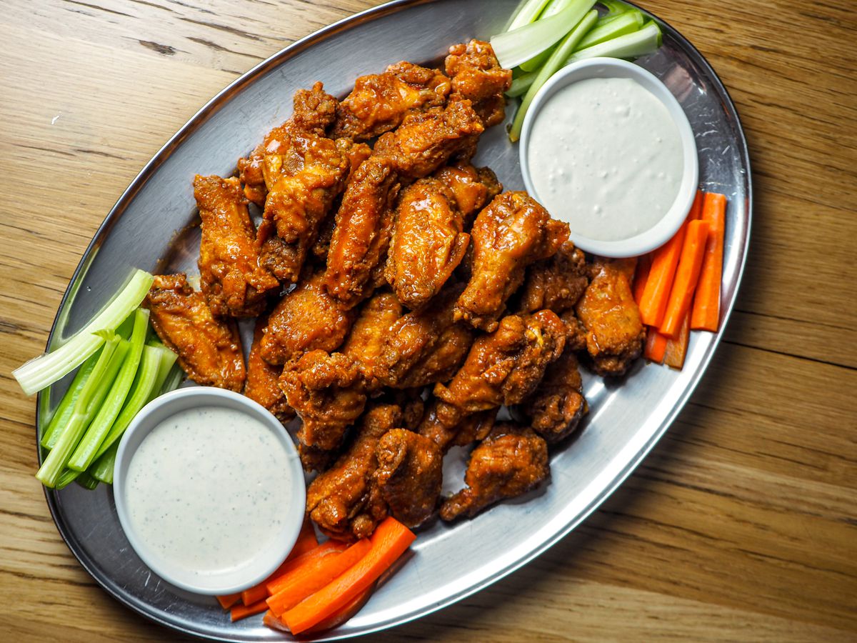A plate of Buffalo wings with celery and carrots and ramekins of ranch dressing.