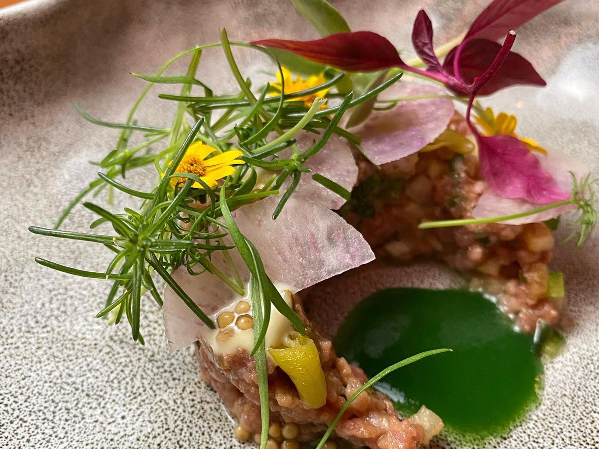 An artful plate of beef tartare with large rosemary sprigs and edible flowers.