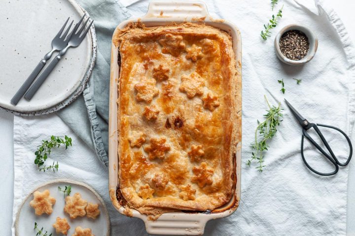 baked chicken and ham pie with golden pastry top, plates next to it ready to serve